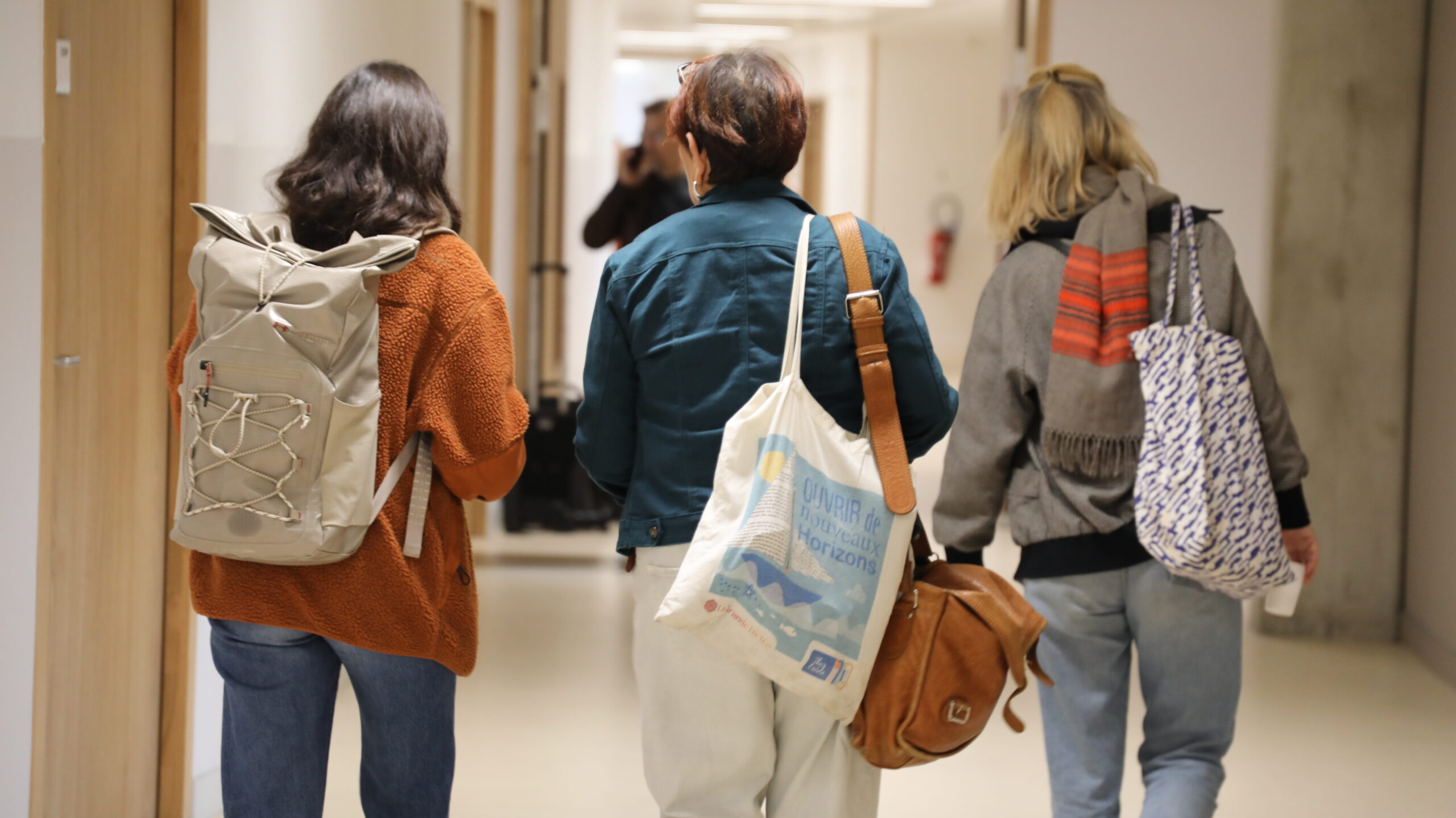 Des enseignantes marchent de dos dans un couloir.